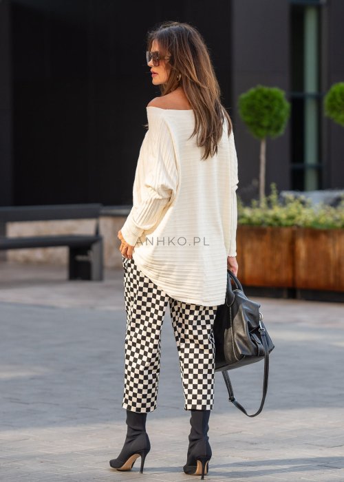 Spodnie damskie w czarno-beżową szachownicę o luźnym kroju z elastycznym pasem i kieszeniami, stylizowane w miejskim looku z koszulą i botkami.