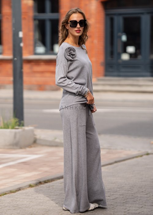 Szary damski sweter z długim rękawem i ozdobną różą na ramieniu, stylizowana z plisowaną różową spódnicą