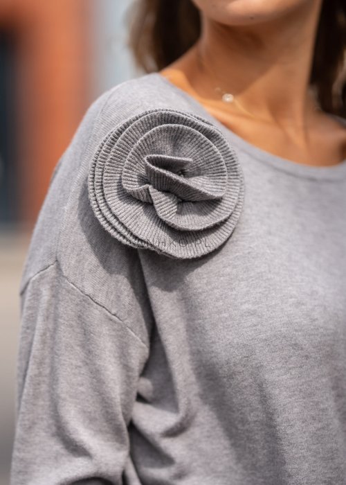 Szary damski sweter z długim rękawem i ozdobną różą na ramieniu, stylizowana z plisowaną różową spódnicą