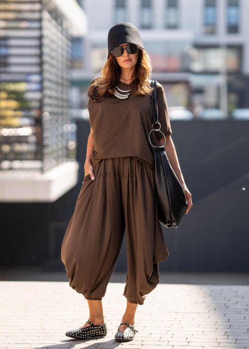 Brązowe spodnie damskie typu harem z szerokimi, drapowanymi nogawkami i elastycznym pasem. Stylizacja z luźnym topem i skórzanymi butami z ćwiekami.