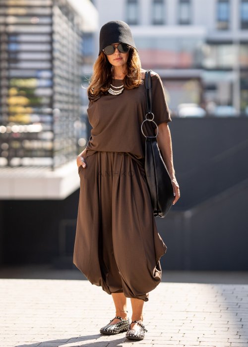 Brązowe spodnie damskie typu harem z szerokimi, drapowanymi nogawkami i elastycznym pasem. Stylizacja z luźnym topem i skórzanymi butami z ćwiekami.