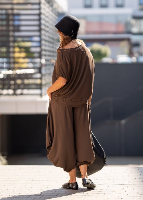 Brązowe spodnie damskie typu harem z szerokimi, drapowanymi nogawkami i elastycznym pasem. Stylizacja z luźnym topem i skórzanymi butami z ćwiekami.