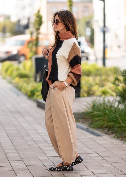 Beżowe spodnie damskie o szerokich nogawkach z efektem bombki i gumką w pasie, zestawione z czarnymi butami z ćwiekami w miejskiej stylizacji.