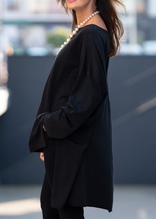 Czarna bluzka oversize z asymetrycznym dołem i dłuższym tyłem, zestawiona z czarnymi spodniami w eleganckiej, miejskiej stylizacji.