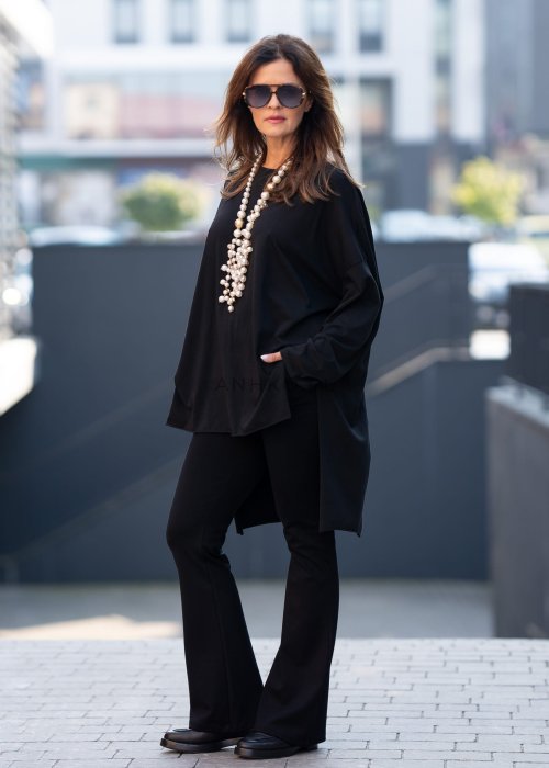 Czarna bluzka oversize z asymetrycznym dołem i dłuższym tyłem, zestawiona z czarnymi spodniami w eleganckiej, miejskiej stylizacji.