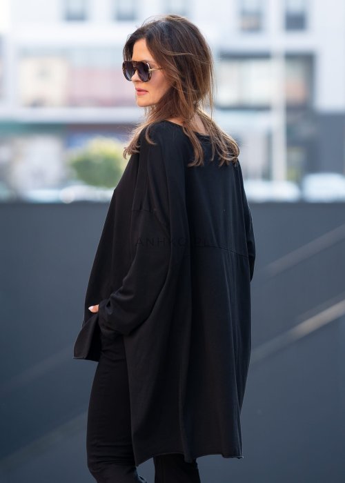 Czarna bluzka oversize z asymetrycznym dołem i dłuższym tyłem, zestawiona z czarnymi spodniami w eleganckiej, miejskiej stylizacji.