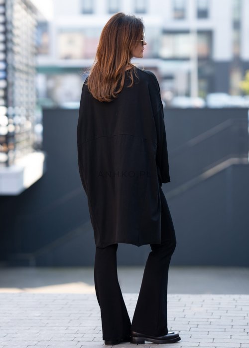 Czarna bluzka oversize z asymetrycznym dołem i dłuższym tyłem, zestawiona z czarnymi spodniami w eleganckiej, miejskiej stylizacji.
