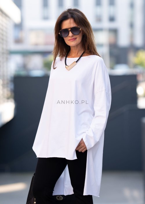 Biała bluzka oversize z dłuższym tyłem i długim rękawem, zestawiona z czarnymi spodniami w minimalistycznej, miejskiej stylizacji.
