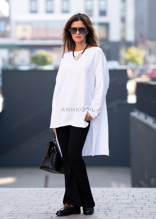 Biała bluzka oversize z dłuższym tyłem i długim rękawem, zestawiona z czarnymi spodniami w minimalistycznej, miejskiej stylizacji.