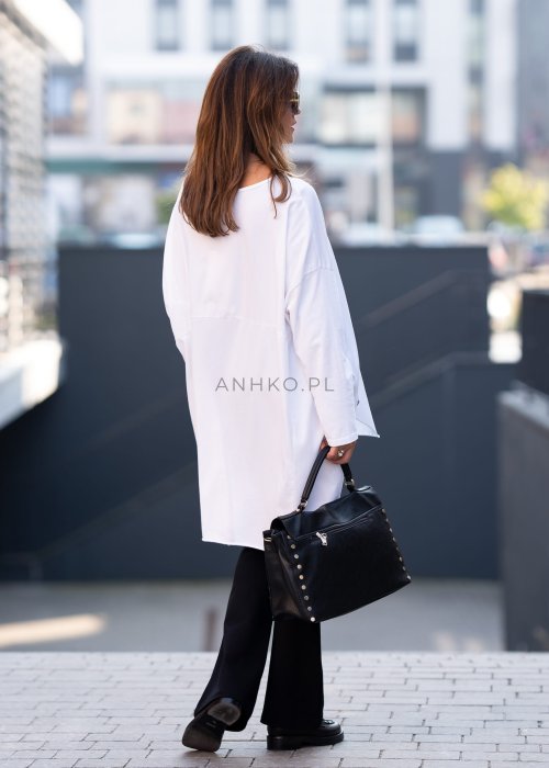 Biała bluzka oversize z dłuższym tyłem i długim rękawem, zestawiona z czarnymi spodniami w minimalistycznej, miejskiej stylizacji.