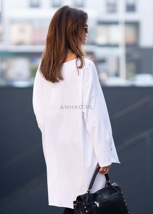 Biała bluzka oversize z dłuższym tyłem i długim rękawem, zestawiona z czarnymi spodniami w minimalistycznej, miejskiej stylizacji.