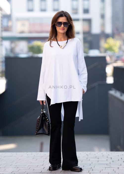 Biała bluzka oversize z dłuższym tyłem i długim rękawem, zestawiona z czarnymi spodniami w minimalistycznej, miejskiej stylizacji.
