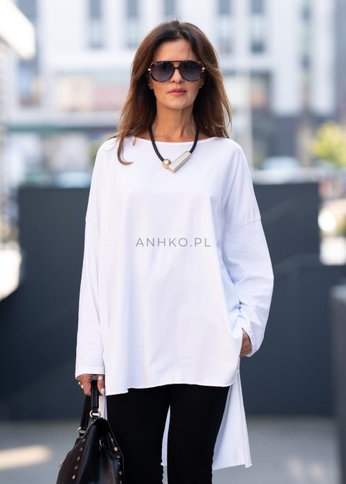 Biała bluzka oversize z dłuższym tyłem i długim rękawem, zestawiona z czarnymi spodniami w minimalistycznej, miejskiej stylizacji.