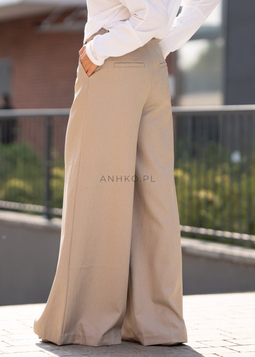 Beżowe spodnie damskie wide leg z wysokim stanem i kopertowym zapięciem, elegancki fason z szerokimi nogawkami w miejskiej stylizacji.