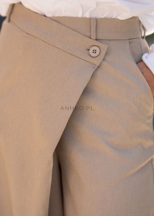 Beżowe spodnie damskie wide leg z wysokim stanem i kopertowym zapięciem, elegancki fason z szerokimi nogawkami w miejskiej stylizacji.