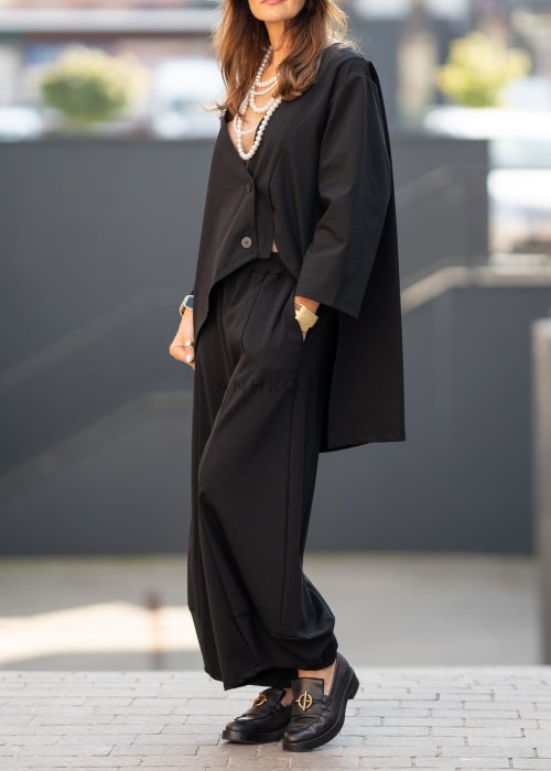 Czarne spodnie damskie o szerokich nogawkach z efektem bombki i elastyczną talią, zestawione z botkami w minimalistycznej stylizacji.