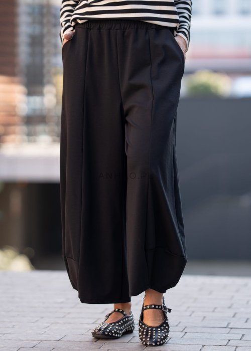 Czarne spodnie damskie o szerokich nogawkach z efektem bombki i elastyczną talią, zestawione z botkami w minimalistycznej stylizacji.