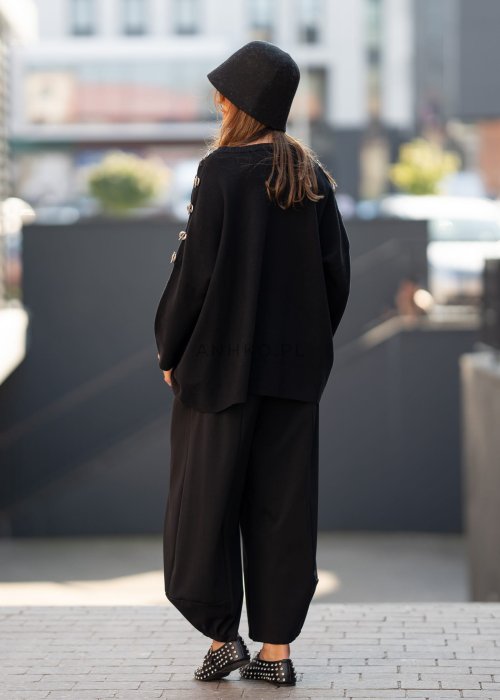 Czarne spodnie damskie o szerokich nogawkach z efektem bombki i elastyczną talią, zestawione z botkami w minimalistycznej stylizacji.