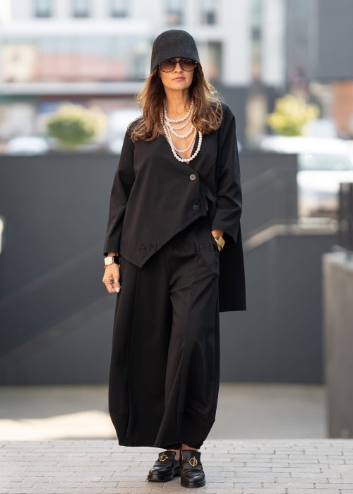 Czarne spodnie damskie o szerokich nogawkach z efektem bombki i elastyczną talią, zestawione z botkami w minimalistycznej stylizacji.