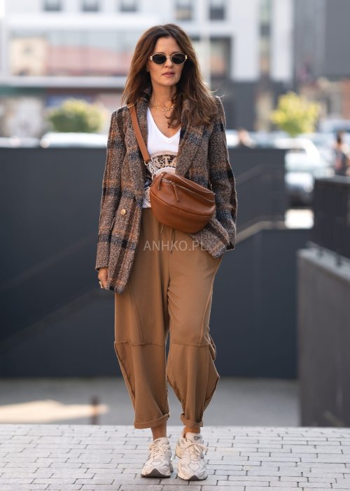 Damskie spodnie dresowe w kolorze camel z fantazyjnymi przeszyciami i elastycznym pasem, stylizowane z jasnymi sneakersami w miejskiej scenerii.