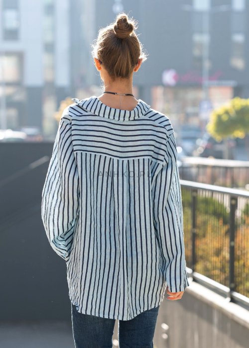 Lniana koszula damska niebieska w paski, luźny fason z kołnierzykiem i guzikami, stylizacja z jeansami i minimalistyczną biżuterią.