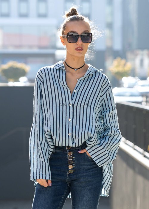 Lniana koszula damska niebieska w paski, luźny fason z kołnierzykiem i guzikami, stylizacja z jeansami i minimalistyczną biżuterią.