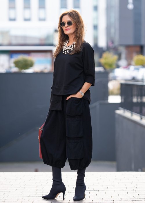 Czarna bluza damska oversize z asymetrycznym dołem i przeszyciami. Model prezentowany w minimalistycznej stylizacji z szerokimi spodniami i biżuterią.