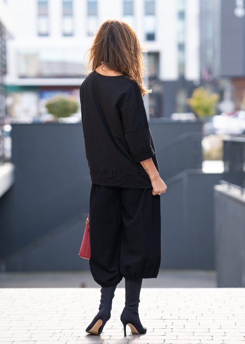 Czarna bluza damska oversize z asymetrycznym dołem i przeszyciami. Model prezentowany w minimalistycznej stylizacji z szerokimi spodniami i biżuterią.