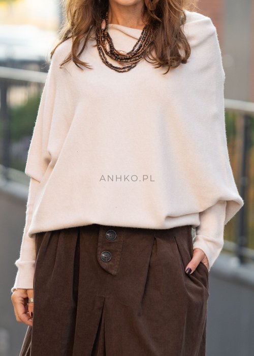 Śmietankowy sweter damski oversize o nietoperzowym kroju z asymetrycznym dołem, stylizacja miejska z szerokimi spodniami.