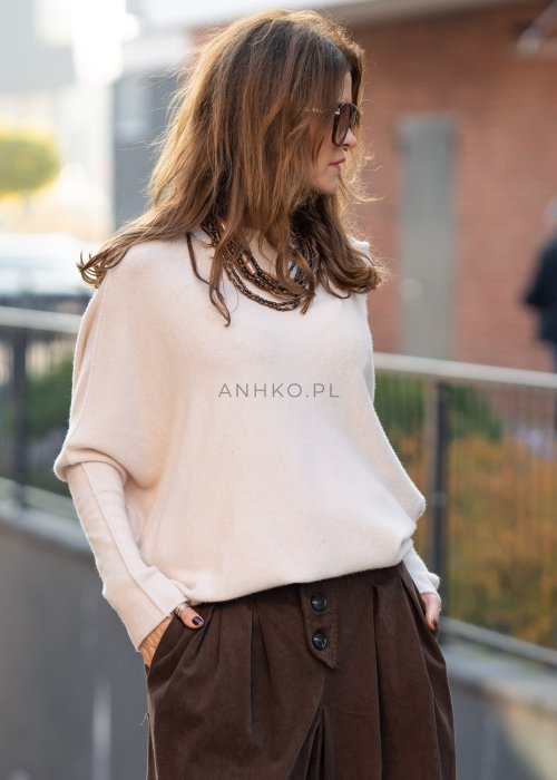 Śmietankowy sweter damski oversize o nietoperzowym kroju z asymetrycznym dołem, stylizacja miejska z szerokimi spodniami.