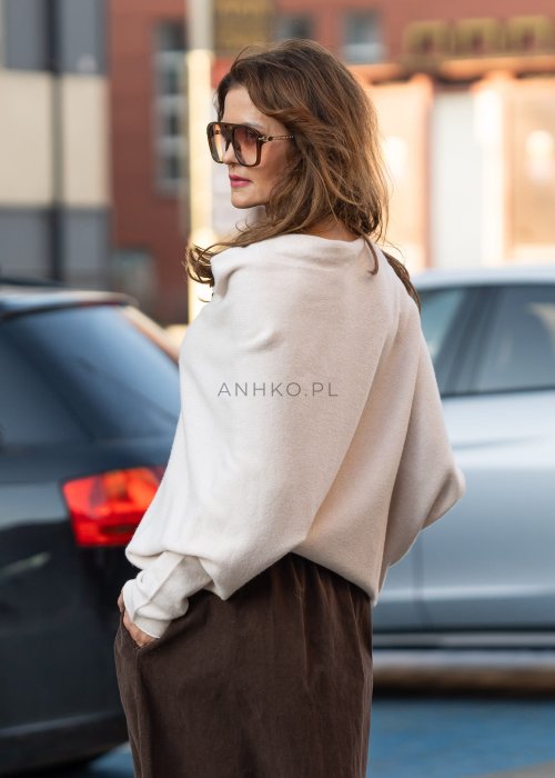 Śmietankowy sweter damski oversize o nietoperzowym kroju z asymetrycznym dołem, stylizacja miejska z szerokimi spodniami.