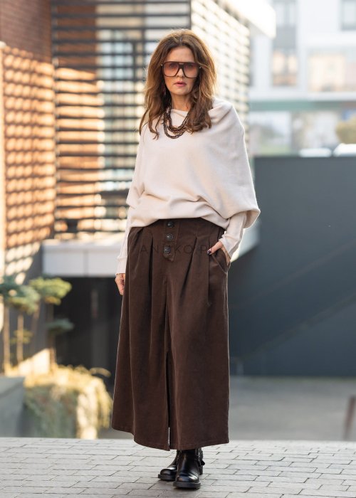 Śmietankowy sweter damski oversize o nietoperzowym kroju z asymetrycznym dołem, stylizacja miejska z szerokimi spodniami.