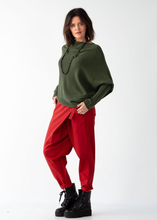 Khaki sweter oversize o nietoperzowym kroju z dekoltem łódka i asymetrycznym dołem zestawiony z czerwonymi szerokimi spodniami i długim naszyjnikiem.