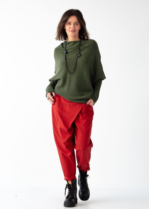 Khaki sweter oversize o nietoperzowym kroju z dekoltem łódka i asymetrycznym dołem zestawiony z czerwonymi szerokimi spodniami i długim naszyjnikiem.
