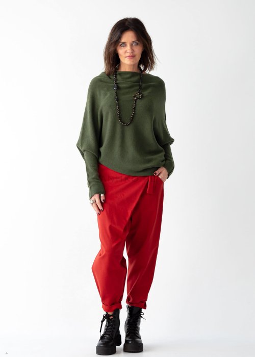Khaki sweter oversize o nietoperzowym kroju z dekoltem łódka i asymetrycznym dołem zestawiony z czerwonymi szerokimi spodniami i długim naszyjnikiem.