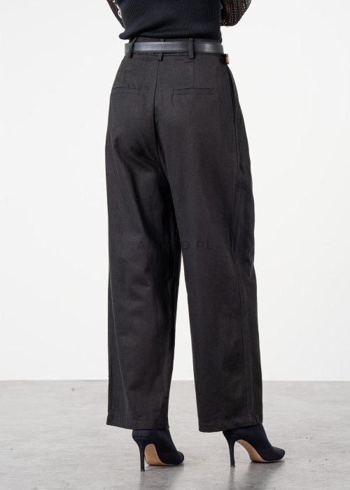 Czarne spodnie damskie z wysokim stanem, zakładkami i paskiem z metalową klamrą. Elegancki model z szeroką nogawką pokazany w stylizacji z dopasowaną górą i botkami na obcasie.