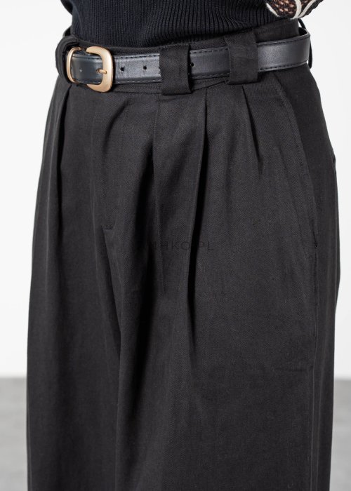 Czarne spodnie damskie z wysokim stanem, zakładkami i paskiem z metalową klamrą. Elegancki model z szeroką nogawką pokazany w stylizacji z dopasowaną górą i botkami na obcasie.