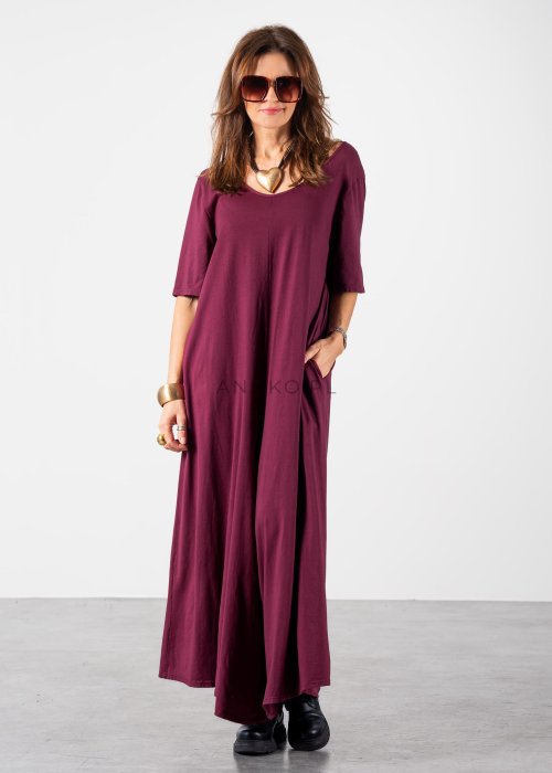 Śliwkowy kombinezon damski oversize z szeroką nogawką i krótkim rękawem, z głębokim wycięciem na plecach w stylizacji z biżuterią i okularami przeciwsłonecznymi.