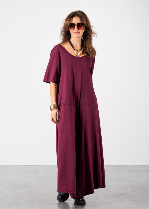 Śliwkowy kombinezon damski oversize z szeroką nogawką i krótkim rękawem, z głębokim wycięciem na plecach w stylizacji z biżuterią i okularami przeciwsłonecznymi.