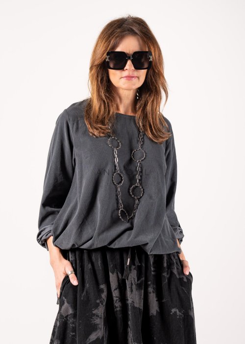 Szara bluzka damska oversize z długim rękawem i regulowanym dołem, minimalistyczny fason w stylizacji z czarną spódnicą midi i botkami.