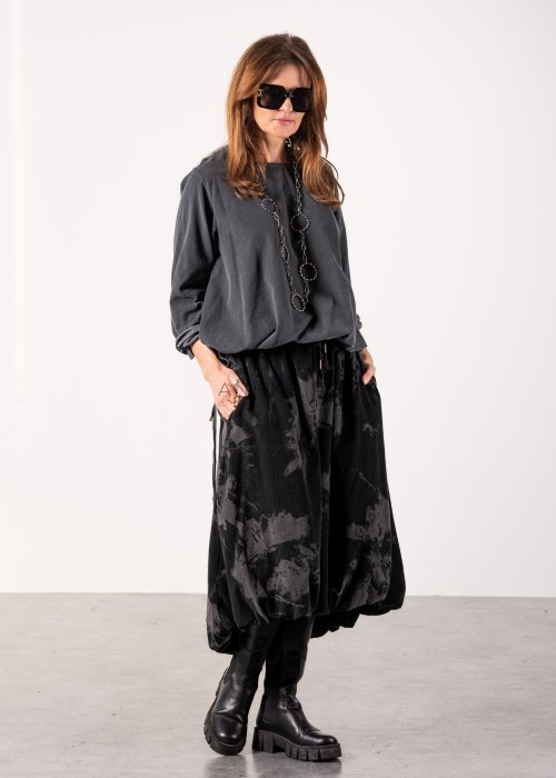 Szara bluzka damska oversize z długim rękawem i regulowanym dołem, minimalistyczny fason w stylizacji z czarną spódnicą midi i botkami.