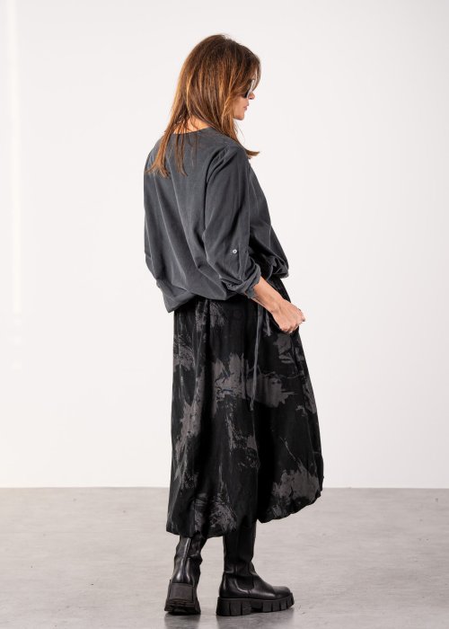 Szara bluzka damska oversize z długim rękawem i regulowanym dołem, minimalistyczny fason w stylizacji z czarną spódnicą midi i botkami.