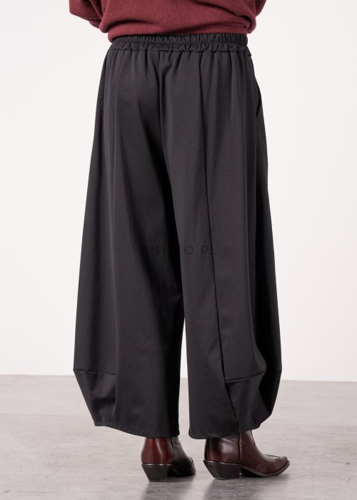 Czarne spodnie damskie o szerokich nogawkach z efektem bombki i elastyczną talią, zestawione z botkami w minimalistycznej stylizacji.