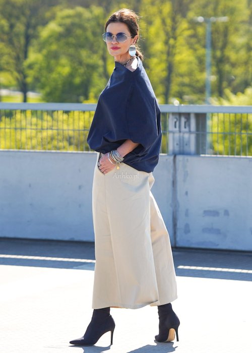 Granatowa bluzka damska oversize z rękawami typu nietoperz i opadającym dekoltem, zestawiona z jasnymi spodniami w eleganckiej stylizacji miejskiej.