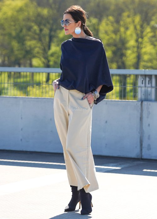 Granatowa bluzka damska oversize z rękawami typu nietoperz i opadającym dekoltem, zestawiona z jasnymi spodniami w eleganckiej stylizacji miejskiej.