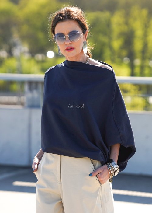 Granatowa bluzka damska oversize z rękawami typu nietoperz i opadającym dekoltem, zestawiona z jasnymi spodniami w eleganckiej stylizacji miejskiej.