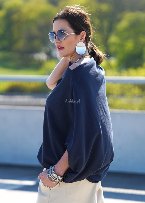 Granatowa bluzka damska oversize z rękawami typu nietoperz i opadającym dekoltem, zestawiona z jasnymi spodniami w eleganckiej stylizacji miejskiej.