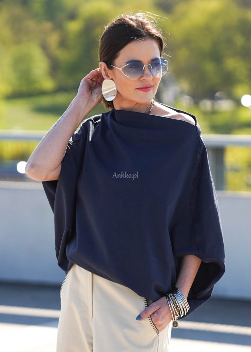 Granatowa bluzka damska oversize z rękawami typu nietoperz i opadającym dekoltem, zestawiona z jasnymi spodniami w eleganckiej stylizacji miejskiej.