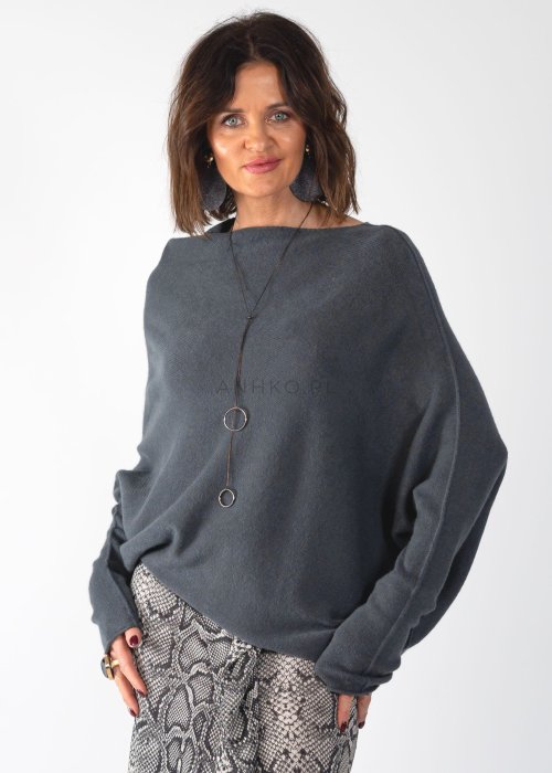 Szary sweter damski oversize o kroju nietoperzowym z dekoltem łódka i asymetrycznym dołem, stylizacja ze spodniami we wzór.