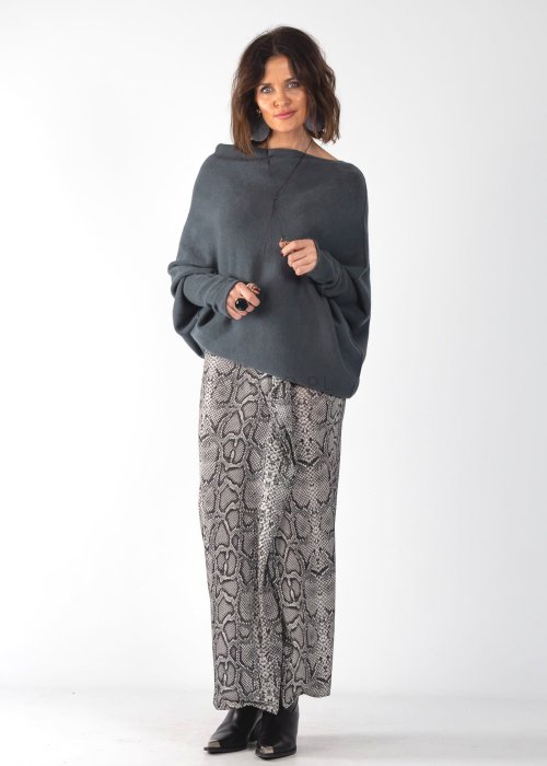 Szary sweter damski oversize o kroju nietoperzowym z dekoltem łódka i asymetrycznym dołem, stylizacja ze spodniami we wzór.